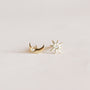 The Sun & Moon features mismatched 18k gold plated stud earrings: one crescent moon with a gemstone and one eight-pointed star with a center stone, displayed on a light background. Perfectly pairs with our Sun & Moon necklace.