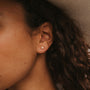 Close-up of a person with curly brown hair and medium skin tone wearing the Sun & Moon 18k gold CZ sunburst stud earring, with a softly blurred background highlighting its celestial-inspired detail.