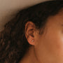 Close-up of a person's ear with long, curly hair, wearing the Sun & Moon stud earring. Most of the background and face are softly blurred.