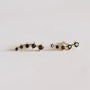 The Black Crawler is a pair of gold earrings with a row of small, round black gemstones set in a curved line, crafted with 18k gold plating and sterling silver posts, shown on a light neutral background.