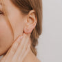 Close-up of a woman's ear wearing the White Crawler—an elegant, curved 18k gold-plated earring with sparkling cubic zirconia. Her hand touches her neck, and her loosely braided hair is set against a softly lit neutral background.