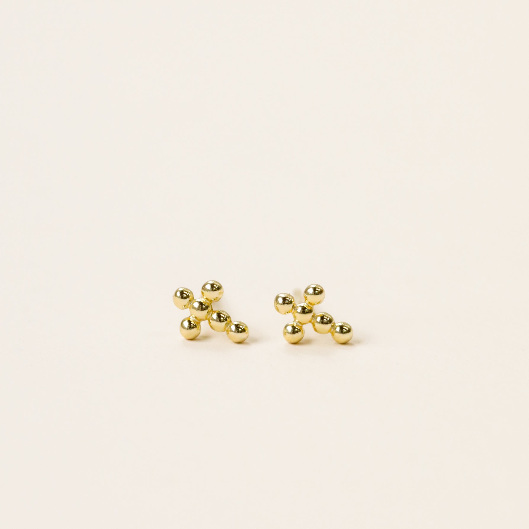 A pair of Cross Stud earrings, small 18k gold plated studs with sterling silver posts shaped like jacks game pieces, shown on a plain light background.