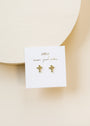 The Cross Stud features small cross earrings with sterling silver posts and 18k gold plating, displayed on a white card with "JaxKelly" and "wear good vibes" in gold lettering, set against a light beige background.