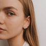 Close-up of a young woman with straight, light brown hair wearing the gold plated Pavé Snake earring—a small, hoop-shaped piece—in her left ear. It glimmers subtly as she faces slightly left with a neutral expression.
