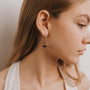 A young woman with long light brown hair wears a white top and the Black Onyx Gemstone Drop - Focus earrings, seen in profile against a neutral background, highlighting her elegant jewelry choice.