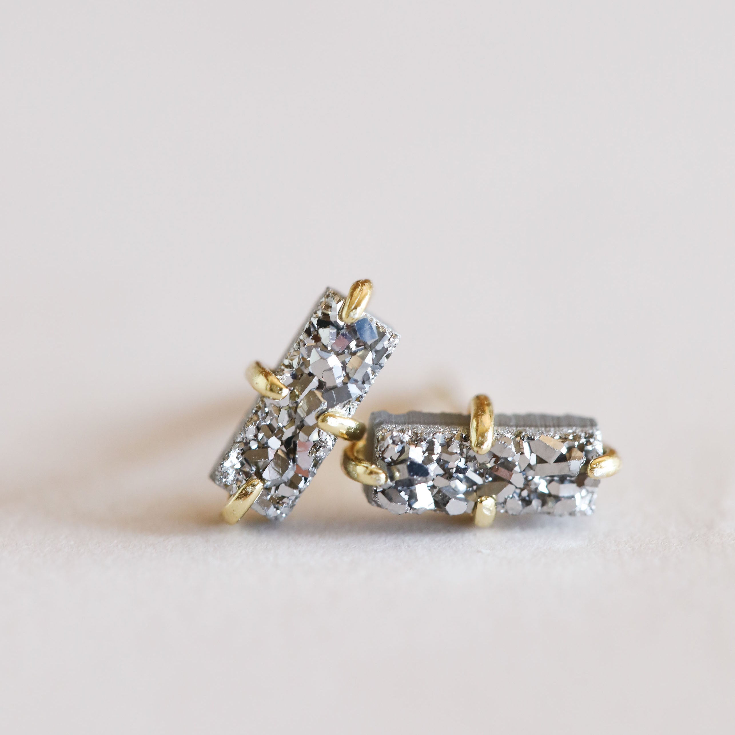 Close-up of Silver Bar Druzy earrings—rectangular studs with sparkling textured sterling silver and 18k gold-plated prongs—set against a soft white background.