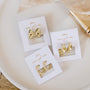 Three pairs of Gold Wide Hoop earrings with a minimalist design are displayed on white cards labeled "JaxKelly wear good vibes," placed on a white plate with a beige cloth and a gold pen nearby.
