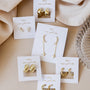 Six pairs of Gold Swirl Hoop earrings are displayed on white Jaycilly cards, set on beige fabric with a glass dish nearby. This collection features stylish, long-lasting hoop designs for an elegant vibe.