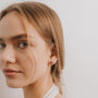A young woman with light brown hair and fair skin wears the Amethyst Gemstone Prong - Healing flower-shaped stud earring, gazing slightly past the camera against a plain white background.