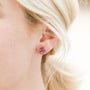 Close-up of a woman wearing the Amethyst Gemstone Prong - Healing earring, her blonde hair pulled back and the background softly blurred.