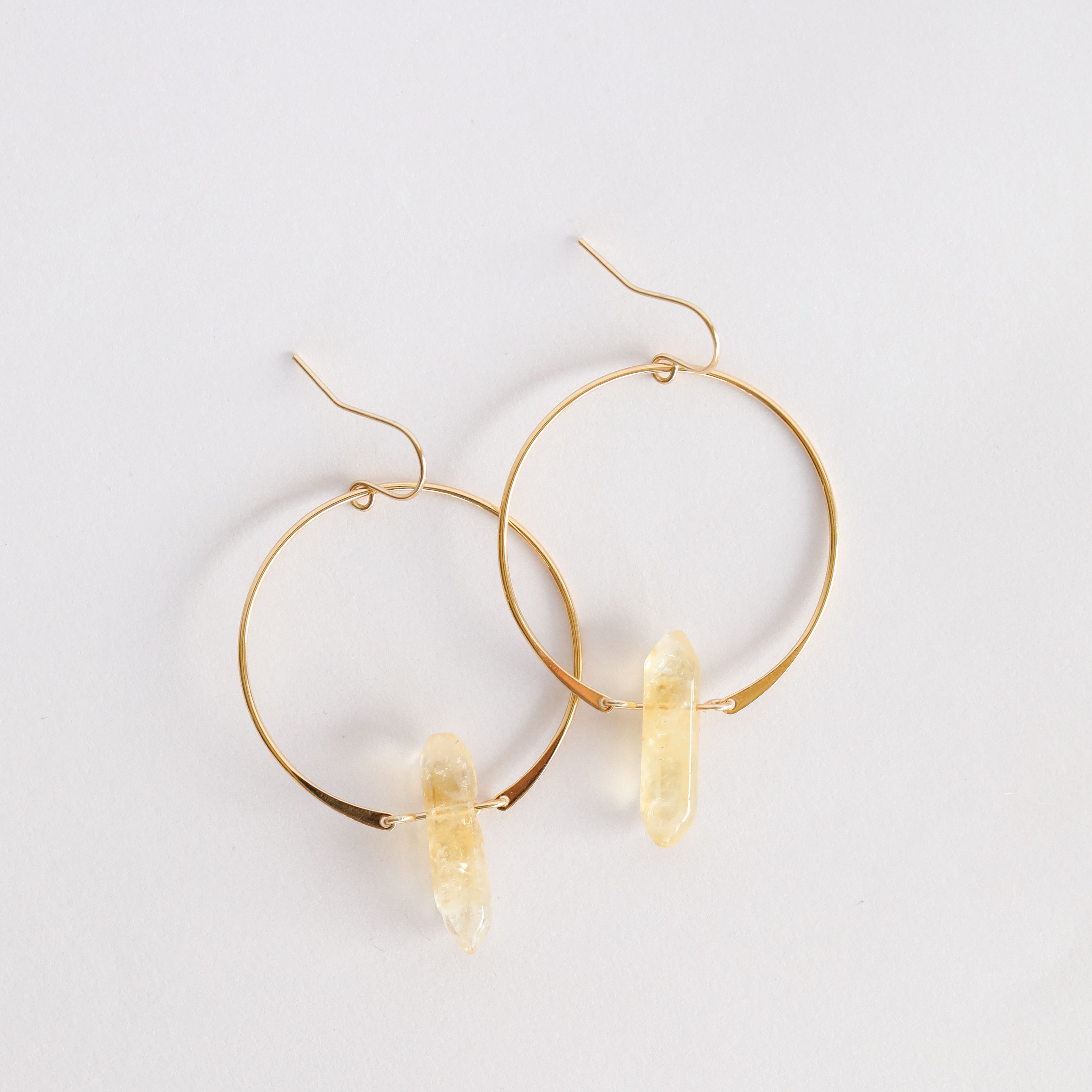 The JaxKelly Citrine Hoop - Success features gold hoops with clear citrine quartz pendants, shown on a white background. These hypoallergenic earrings offer everyday elegance and style.