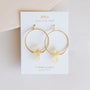 A pair of hypoallergenic gold Citrine Hoop - Success earrings from JaxKelly, featuring citrine quartz crystals and displayed on a white card labeled "Wear Good Vibes," "Citrine Quartz," and "success stone.