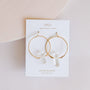 The Clear Quartz Hoop - Healing earrings feature gold hoops with clear quartz stones, displayed on a white JaxKelly card labeled "Wear Good Vibes - Clear Quartz Healing Stone" against a light neutral background.