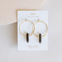 The Smoky Quartz Hoop - Protection earrings, featuring gold hoops with smoky quartz pendants, are displayed on a white JaxKelly card against a light, neutral background.