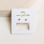 The Gold Sphere Huggie, featuring 18k gold plating, is displayed on a white JaxKelly card with "wear good vibes" in gold lettering, propped on a light surface.