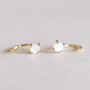A delicate pair of Mother of Pearl Huggie gold rings, each with a small round white stone in a four-prong setting, displayed on a light neutral background.