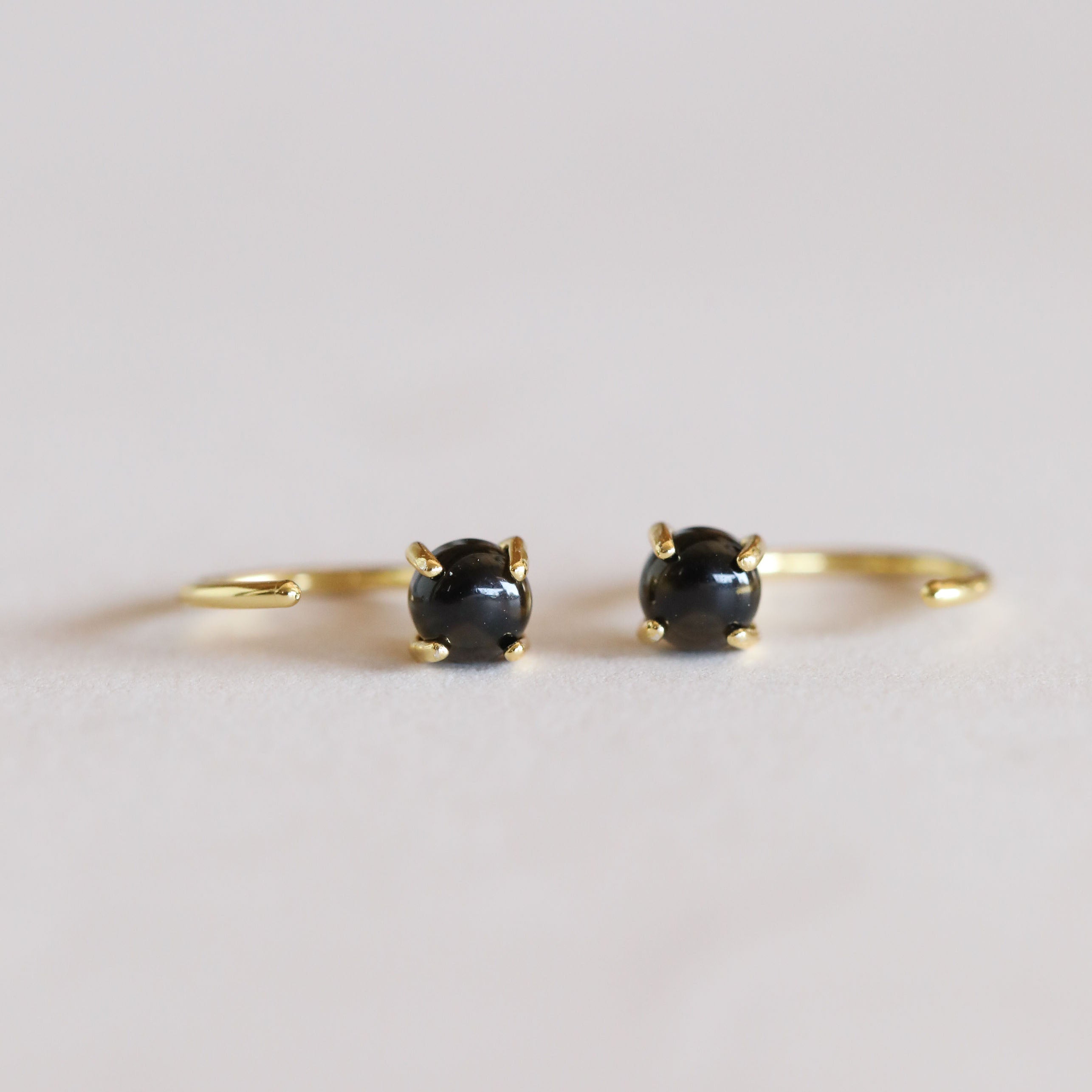 The Obsidian Huggie showcases round Obsidian gemstones in a four-prong setting with 18k gold plating, displayed on a light neutral background.
