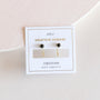 Obsidian Huggie earrings with 18k gold plating and Obsidian gemstone studs, displayed on a white JaxKelly Gemstone Huggies card labeled "Obsidian—block negativity," set on a soft pink and white background.
