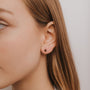 Close-up of a woman's ear with straight light brown hair, wearing the Obsidian Huggie: a small, round black earring featuring an obsidian gemstone in her pierced earlobe. The softly blurred background creates a neutral setting.