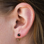 Close-up of an ear wearing the Obsidian Huggie: a dainty 18k gold-plated hoop in the lower lobe, with a gold stud featuring a dark obsidian gemstone above. Light brown hair is partially visible.