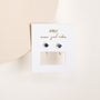 The Sapphire CZ Huggie earrings feature deep blue cubic zirconia stones and 18k gold plating, displayed on a JaxKelly card with "more good vibes," set against a clean, minimalist background.