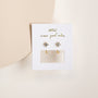 The White CZ Huggie gold plated earrings with crystal studs are displayed on a JAXXELLY card reading "wear good vibes," set against a soft beige background.
