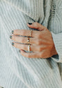 A close-up of a hand with black nail polish, wearing the Ridged Ring—an 18k gold-plated, stackable band—resting on a textured light grey sweater.