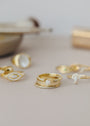 A close-up of the Celestial Ring, featuring intricate gold designs with gemstones and cubic zirconia, shines against a softly blurred background alongside other delicate gold jewelry.