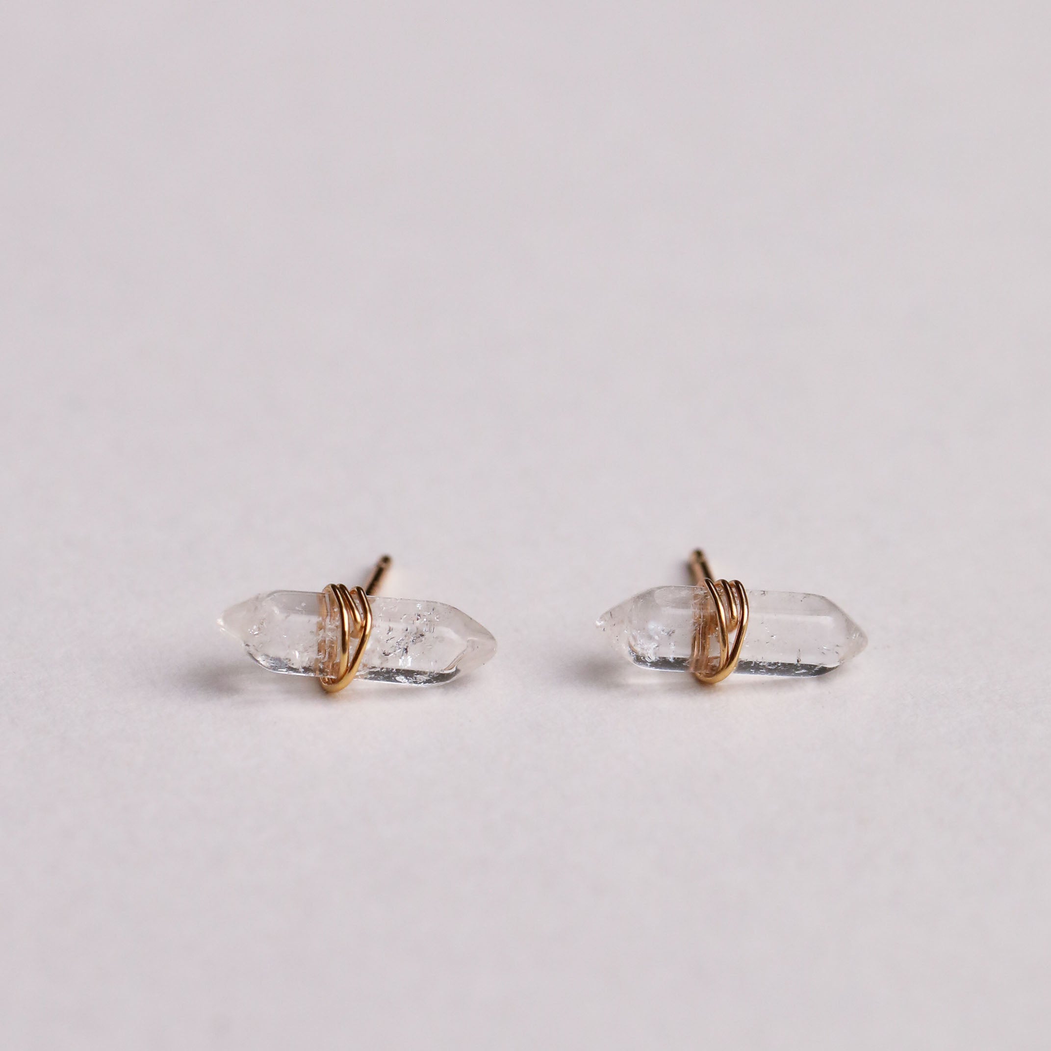 A Clear Quartz Mineral Point for cleansing, featuring polished gemstones and gold wire wrapping, is displayed on a plain white background.