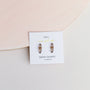 The Smoky Quartz Mineral Point - Protection earrings, set in sterling silver, are showcased on a white card with gold and black text, placed against a light background with a textured circular accent in the corner.