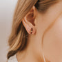 Close-up of a woman's ear adorned with the Smoky Quartz Mineral Point - Protection earring, featuring a small oval stud with an 18k gold plated band. Her light brown hair is tucked behind her ear, highlighting her smooth fair skin.