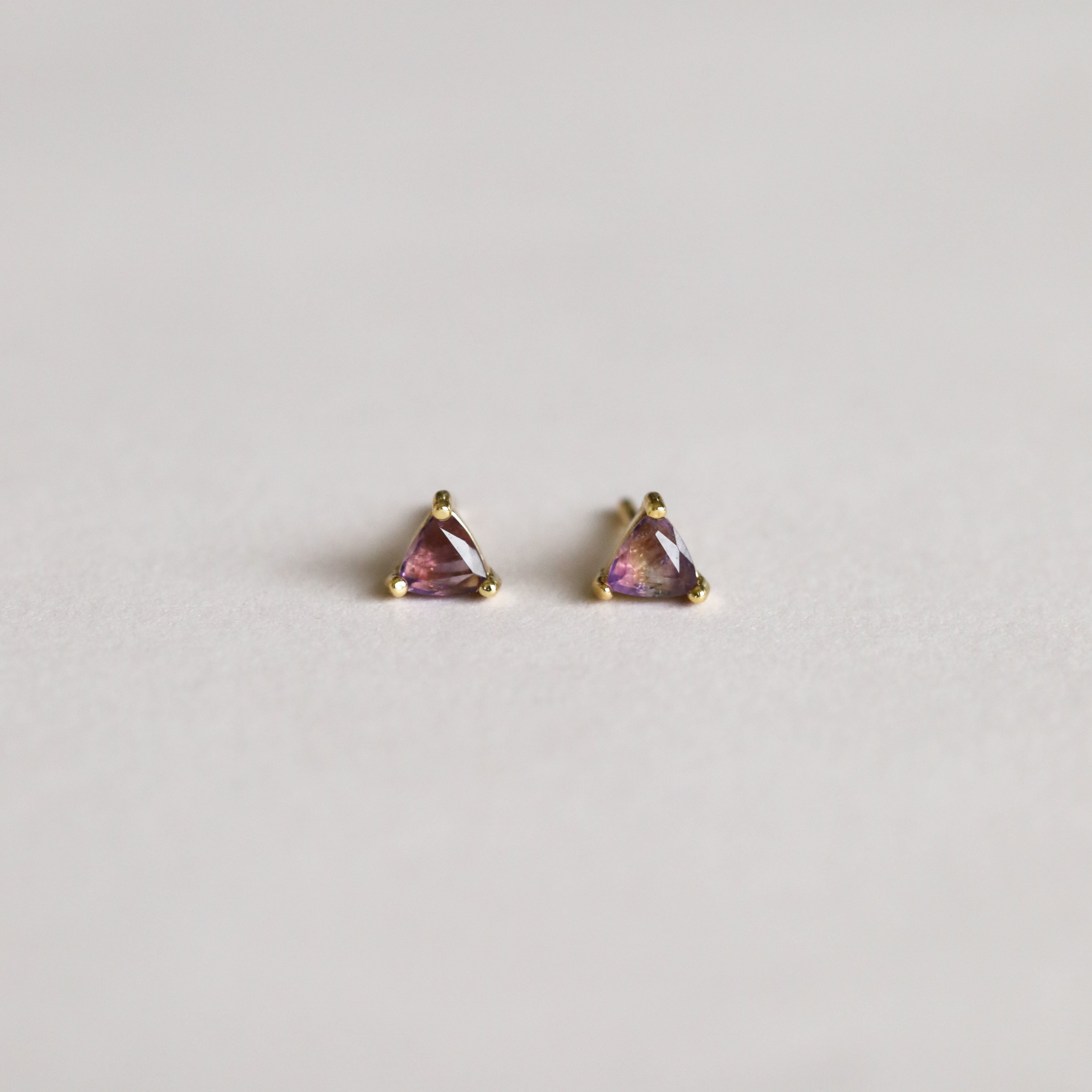 A pair of Amethyst Mini Energy Gems - Healing: small gold stud earrings with triangular purple gemstones and sterling silver posts, shown on a plain light background.