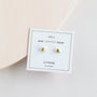A pair of small, gold, triangle-shaped Citrine - Mini Energy Gems - Success studs with sterling silver posts and 18k gold plating are displayed on a white JaxKelly card against a pale background.