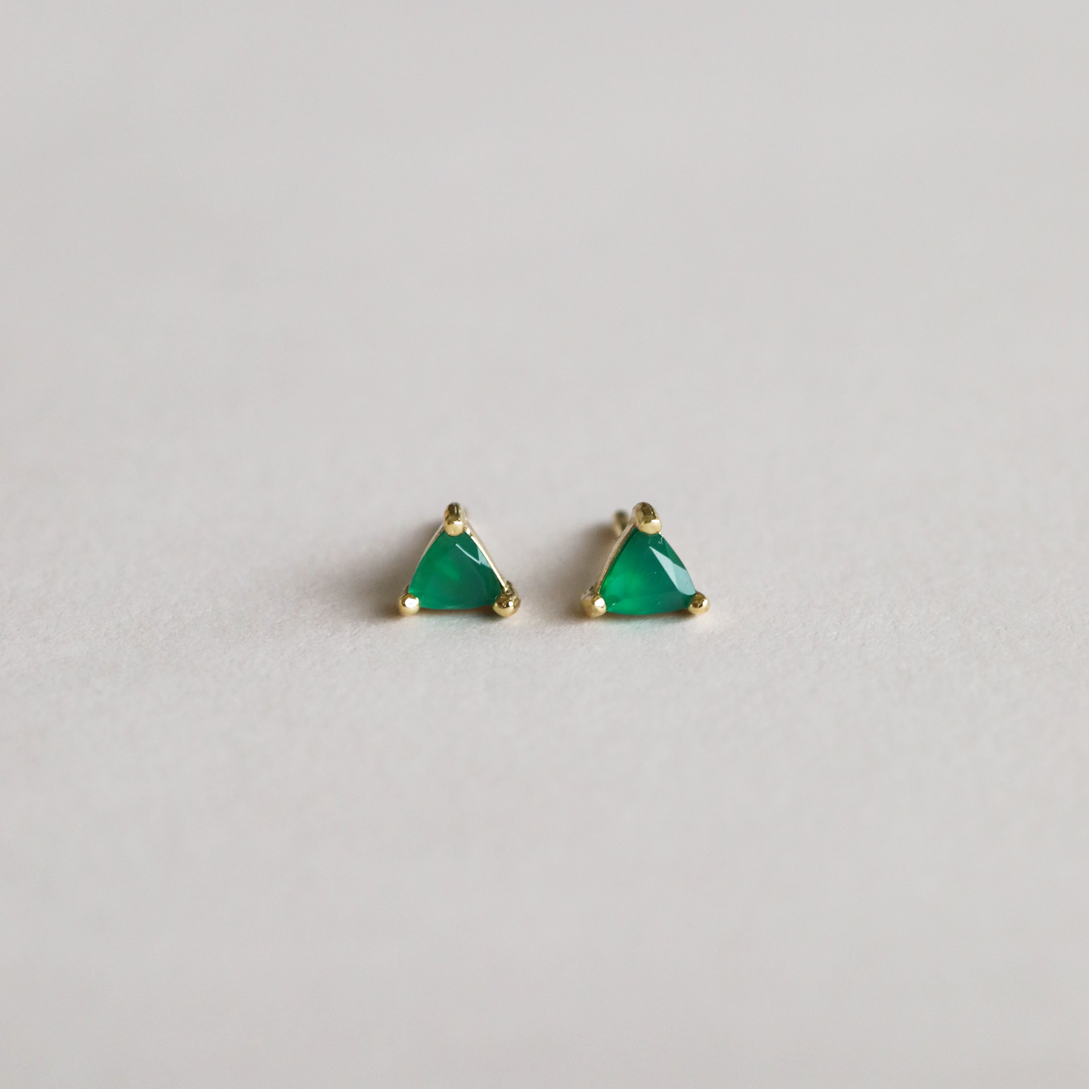 A pair of Green Onyx Mini Energy Gems - Abundance, featuring green onyx triangular stones set in 18k gold plated studs, displayed on a plain light surface.