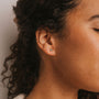 Close-up of a person's ear with Green Onyx Mini Energy Gems - Abundance studs. Their curly hair frames their face, eyes closed and skin smooth, expressing peace.