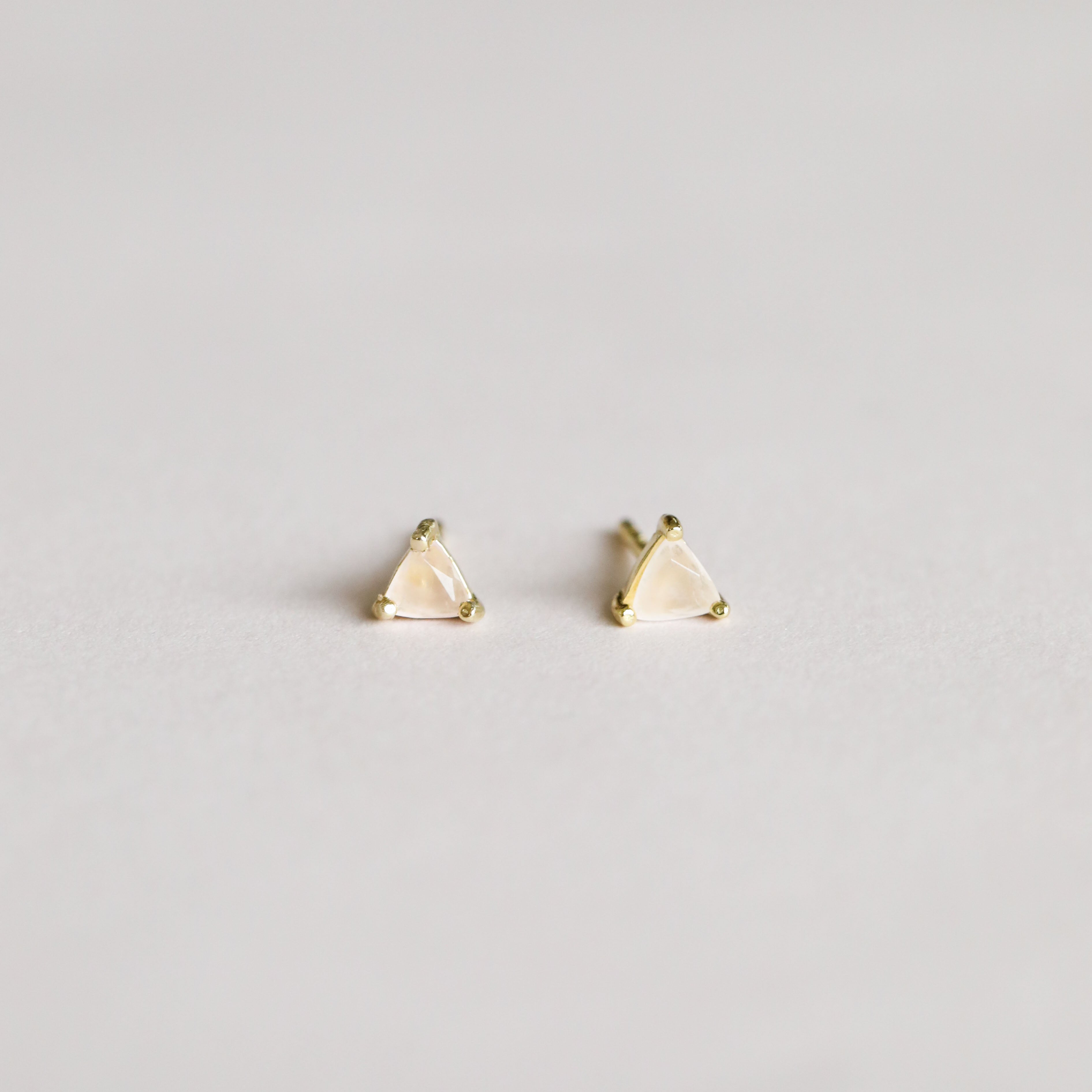 A pair of Rose Quartz Mini Energy Gems - Love: small, triangular studs with 18k gold plating and translucent rose quartz stones on sterling silver posts, displayed against a simple light background.