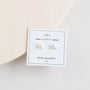 The Rose Quartz Mini Energy Gems - Love are small, triangle-shaped rose quartz studs with sterling silver posts, displayed on a card reading "MINI ENERGY GEMS ROSE QUARTZ love" against a minimal background.