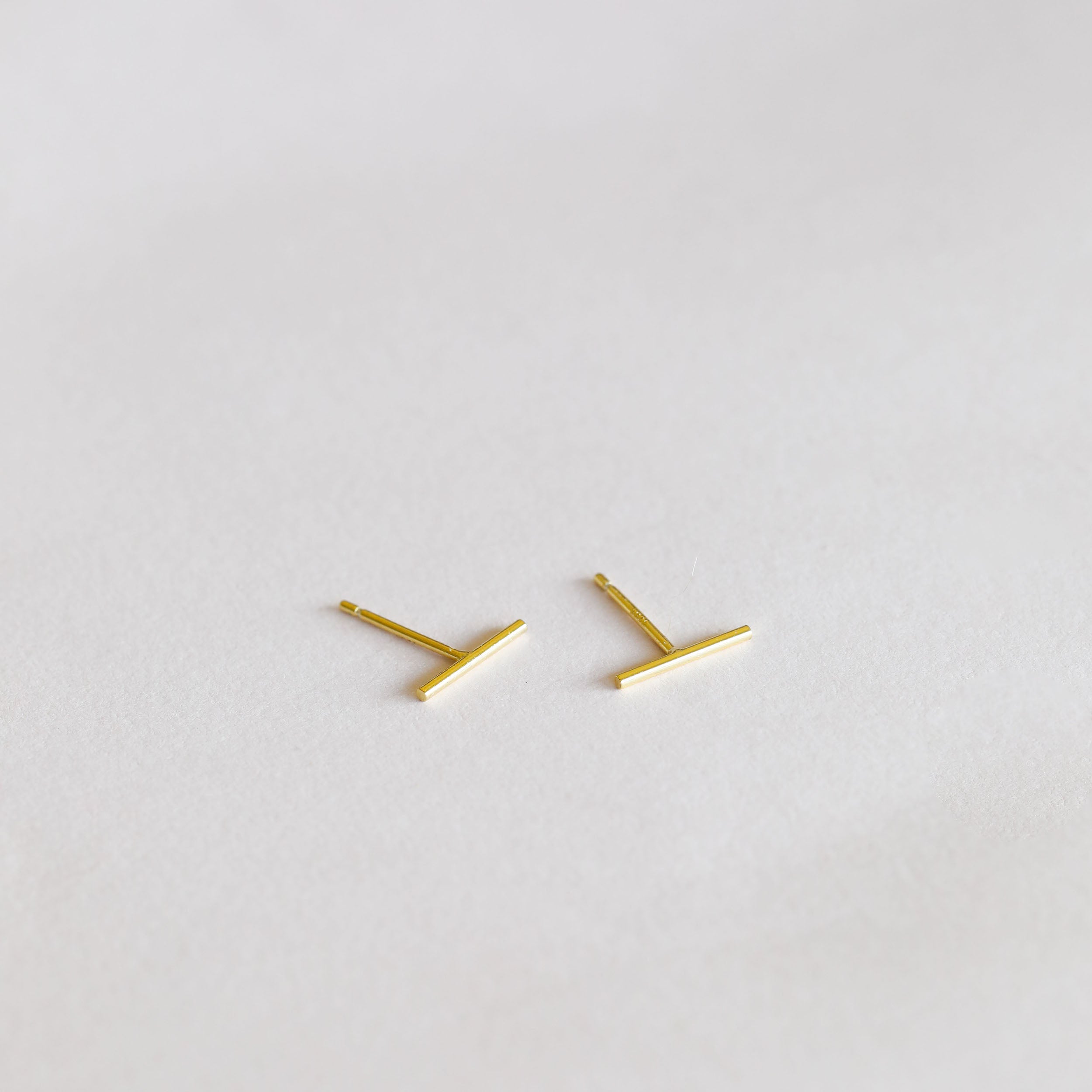 The Minimalist Bar earrings, crafted in 18k gold plated sterling silver, are shown on a soft, light-colored background.