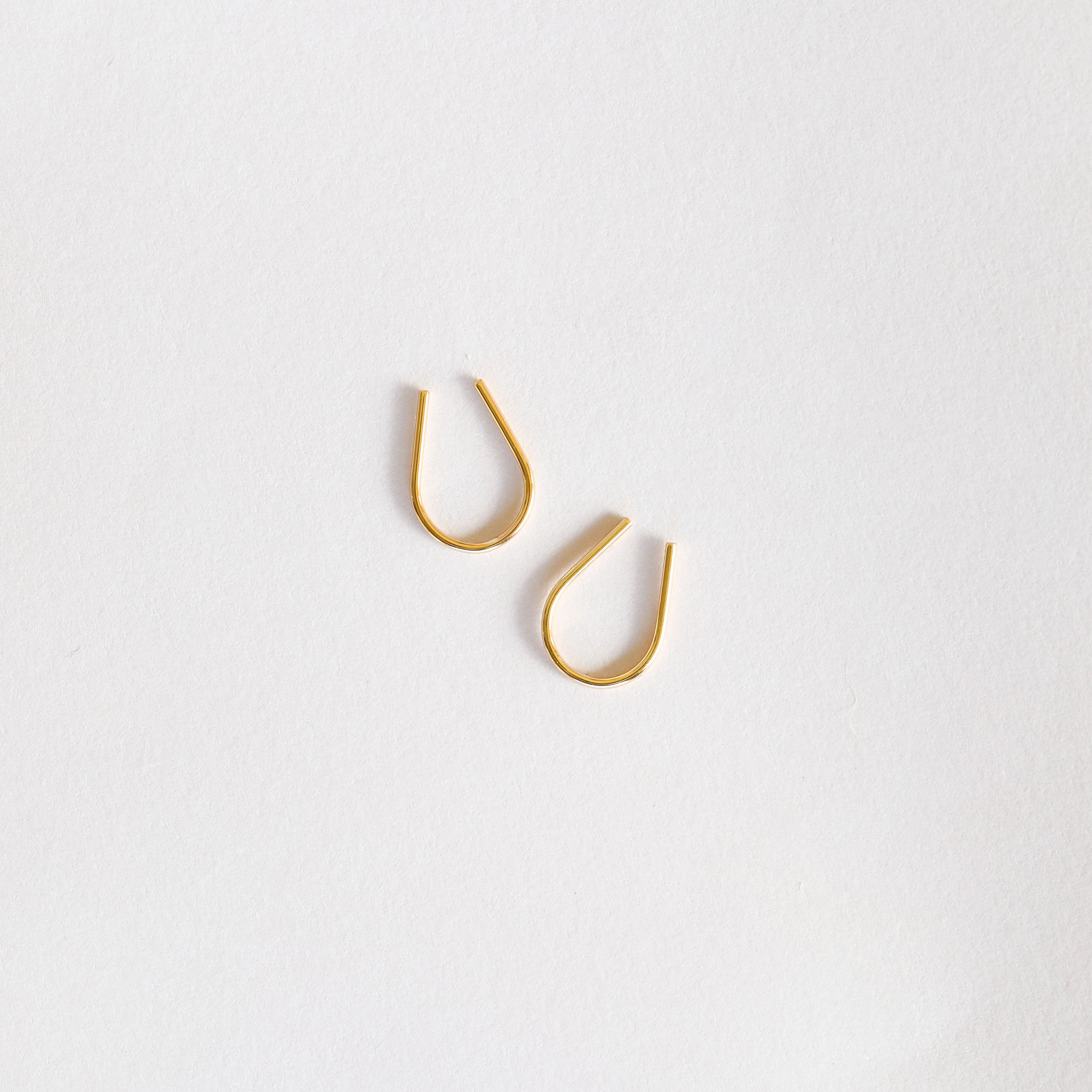 A pair of Minimalist Horseshoe earrings, crafted with 18k gold plating and a teardrop-shaped hoop design, are displayed on a plain white background.