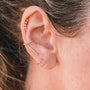 Close-up of an ear with multiple piercings wearing gold and diamond earrings, highlighted by the Minimalist Spiral—a spiral earring with 18k gold plating—adorned along the lobe, helix, and cartilage. Brown hair gently frames the ear.