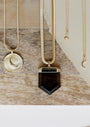 Four gold necklaces rest on a wooden and beige fabric surface, featuring an 18k gold plated crescent moon pendant, a CZ stone pendant, a Cubic Zirconia sun charm, and the Tiny Star Necklace.