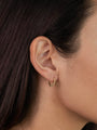 A close-up of a woman wearing the Small Ball Hoop: gold plated earrings featuring small ball details. Her straight dark hair is tucked back, highlighting the hoops. Sterling silver posts offer comfort and quality.
