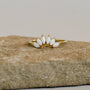 The Opal Crown Ring features five marquise-cut white opals in a graceful curve, set on an 18k gold plated band. Shown on a textured stone, it's an elegant piece ideal for stacking collections.