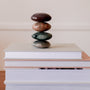 The Moonstone Palm Stone - Luck, a genuine crystal with a smooth, colorful finish, is stacked atop books against a neutral backdrop—an inviting accent for your manifestation practice.
