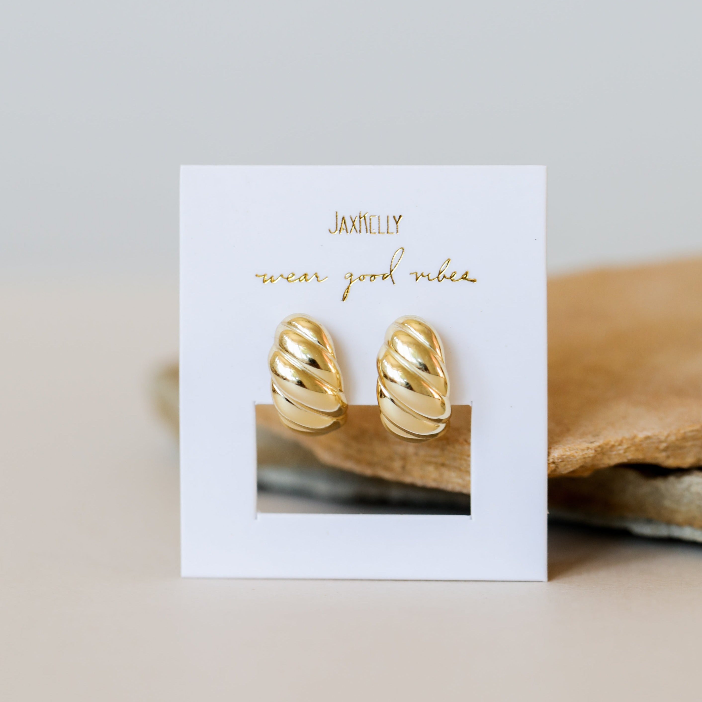 The Gold Swirl Hoop earrings, featuring a shiny gold-plated twisted design, are displayed on a JaxKelly "wear good vibes" card with a neutral background—ideal for those seeking stylish, long-lasting jewelry.