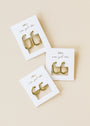 Three pairs of gold hoop earrings, including the Small Rectangular Hoop with gold plating and sterling silver posts, are displayed on white JaxKelly cards reading “wear good vibes” against a neutral beige background.