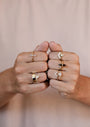 Two fists side by side, each hand wearing several Simple Stud Rings—18k gold plated with unique designs like a sun, triangles, and geometric shapes—set against a neutral background.