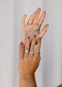 Two hands with brown nail polish and various gold rings, including the elegant Opal Crown Ring, are held up against a light background. The graceful, overlapping fingers show off both the featured ring and delicate stacking styles.