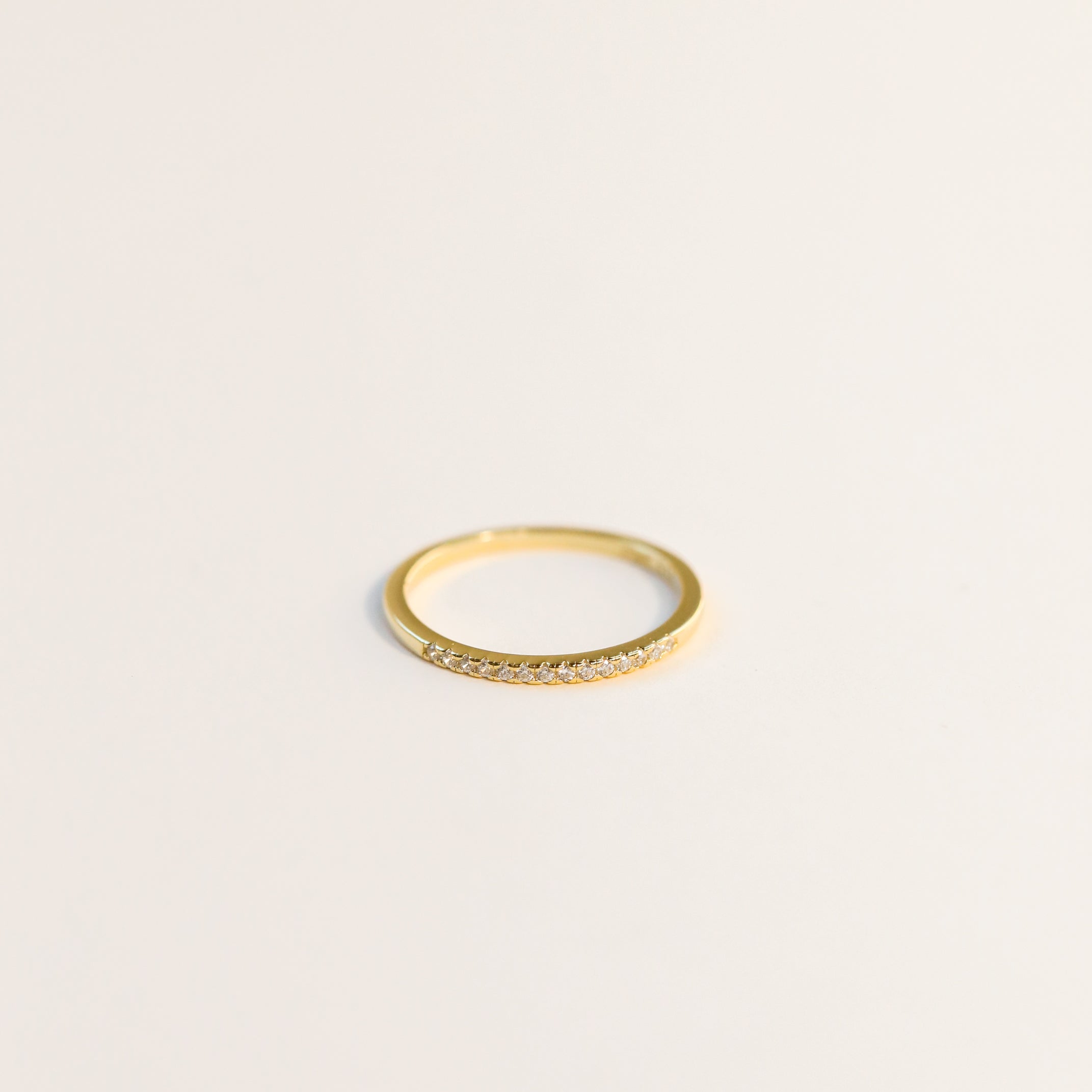 The Half Pavé Ring is a delicate, minimalist gold-plated ring featuring small cubic zirconia stones across the top, showcased on a plain light background.