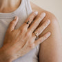 A close-up of a hand wearing the Lambda Ring—one gold-plated ring with a small stone and one black ring—resting on the shoulder of someone in a sleeveless, light gray ribbed top.